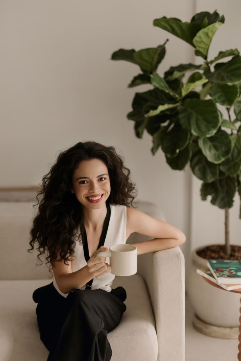 Isabele Fernandes, psicóloga, sorrindo e segurando uma xícara em um ambiente acolhedor