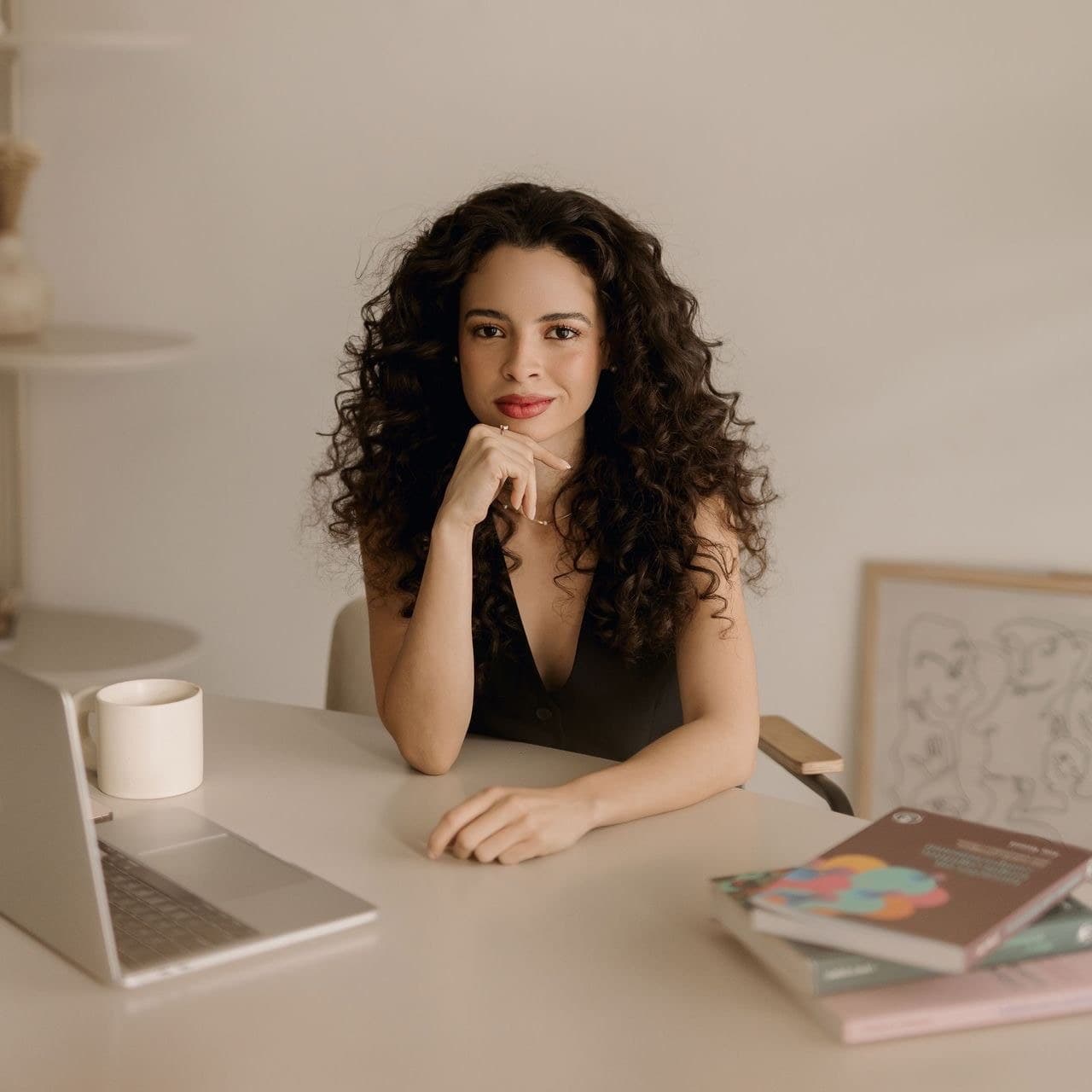 Isabele Fernandes sentada à mesa, com a mão apoiada no queixo, olhando para a câmera